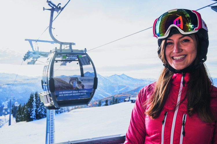 Lächelnde Skifahrerin sitz in einer Gondel.