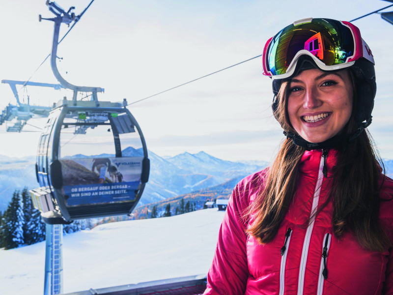 Lächelnde Skifahrerin sitz in einer Gondel.