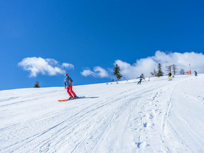 Mehrere Skifahrer fahren eine sonnige Piste hinunter.
