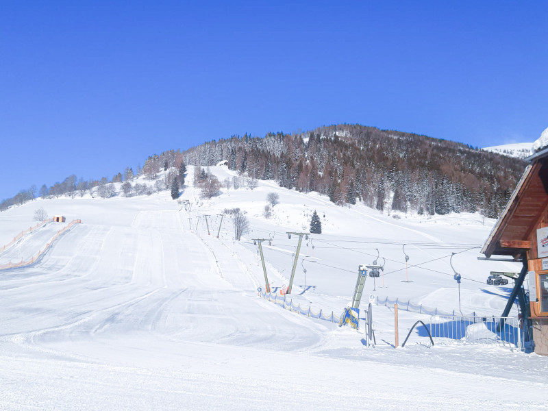„Sonniger Wintertag im Skigebiet Krakau mit frisch präparierten Skipisten, Schleppliften und erschneiten Hängen vor blauem Himmel.