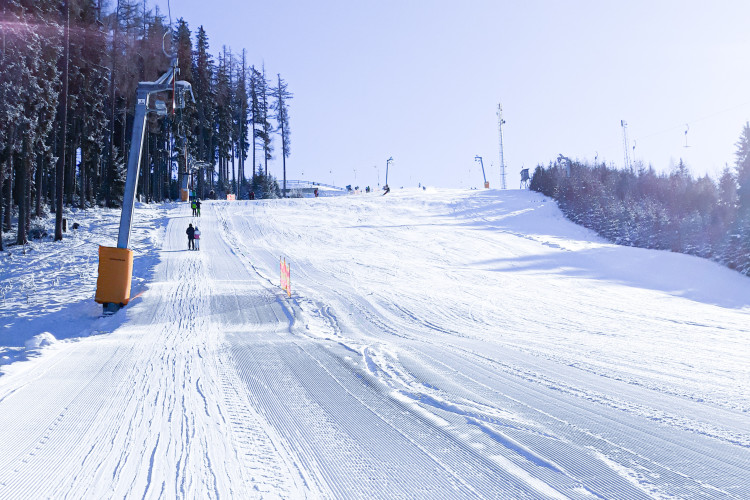 Frisch präparierte Skipiste mit Schlepplift, umgeben von verschneiten Bäumen und sonnigem Winterhimmel.