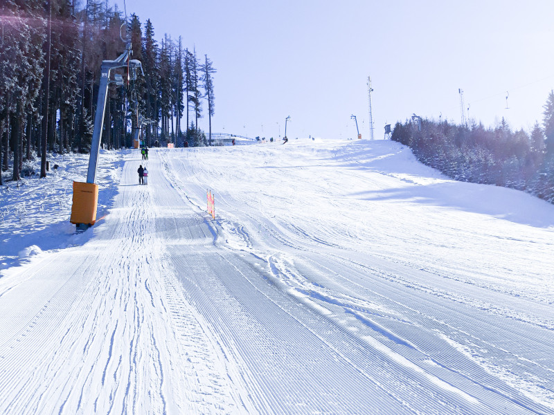 Frisch präparierte Skipiste mit Schlepplift, umgeben von verschneiten Bäumen und sonnigem Winterhimmel.