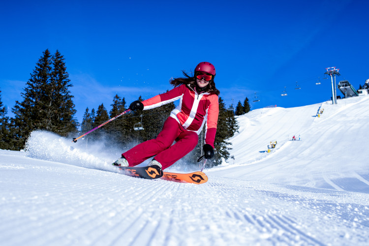 Frau in roter Skibekleidung fährt dynamisch eine sonnige Skipiste hinunter.